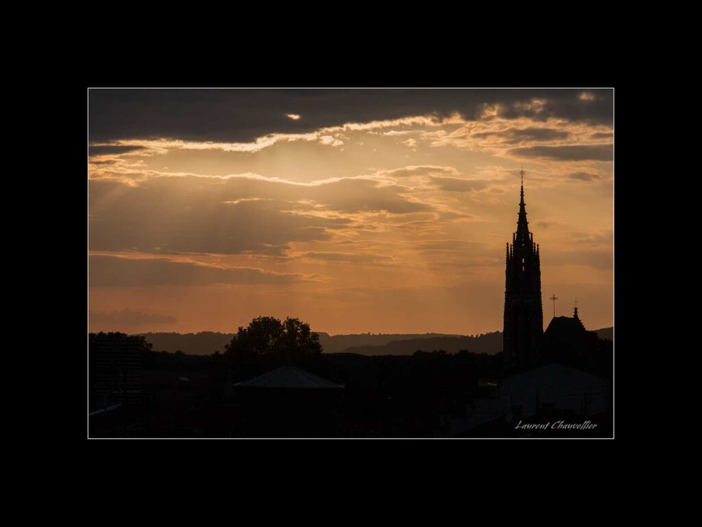 Cathédrale Saint-Caprais d'Agen en contre jour avec un ciel nuageux couleur orange et doré et des rayons qui transpercent les nuages
